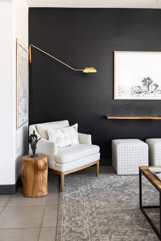 Desert eclectic living room design with white accent chair, wood stump side table, and black feature wall.