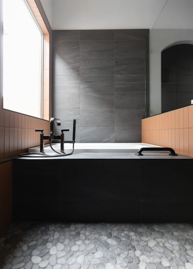 Built in bathtub with matte black grab bar on a orange tiled wall, showcasing accessible and stylish bathroom design by Blue Copper Design.