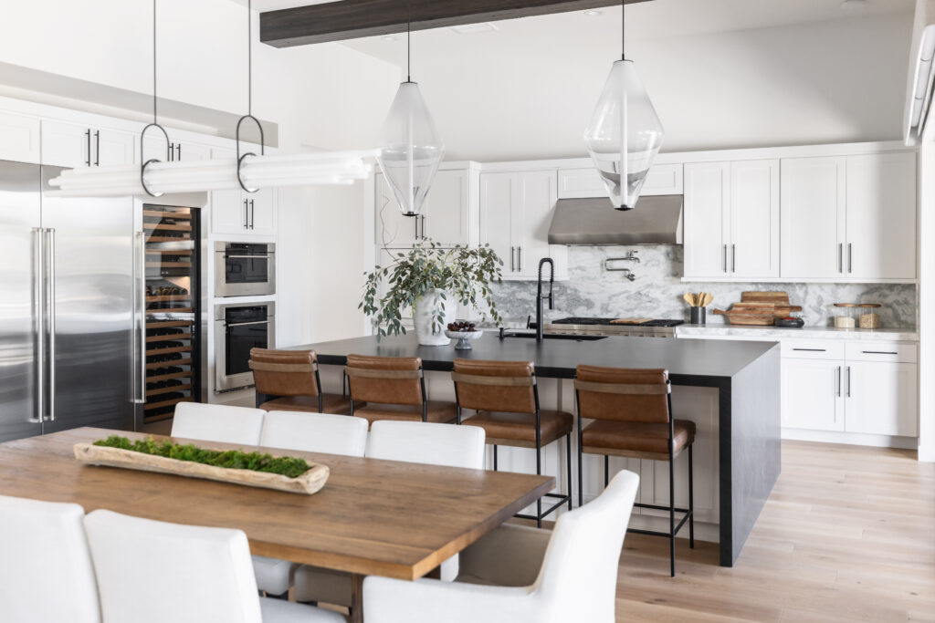 Open concept luxury kitchen and dining room with white cabinets, black countertops and luxury light fixtures.