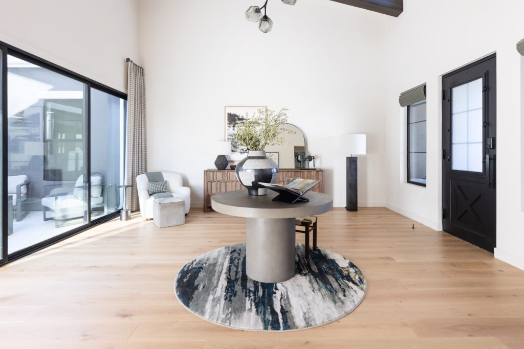 Large entryway with circle rug and concrete table on the rug. Teh concrete table is decorated with a large pot with branches and open book. 