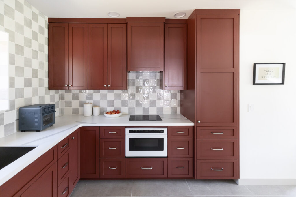 Kitchenette in a casita with white and grey checkered tile backsplash and red cabinetry. 