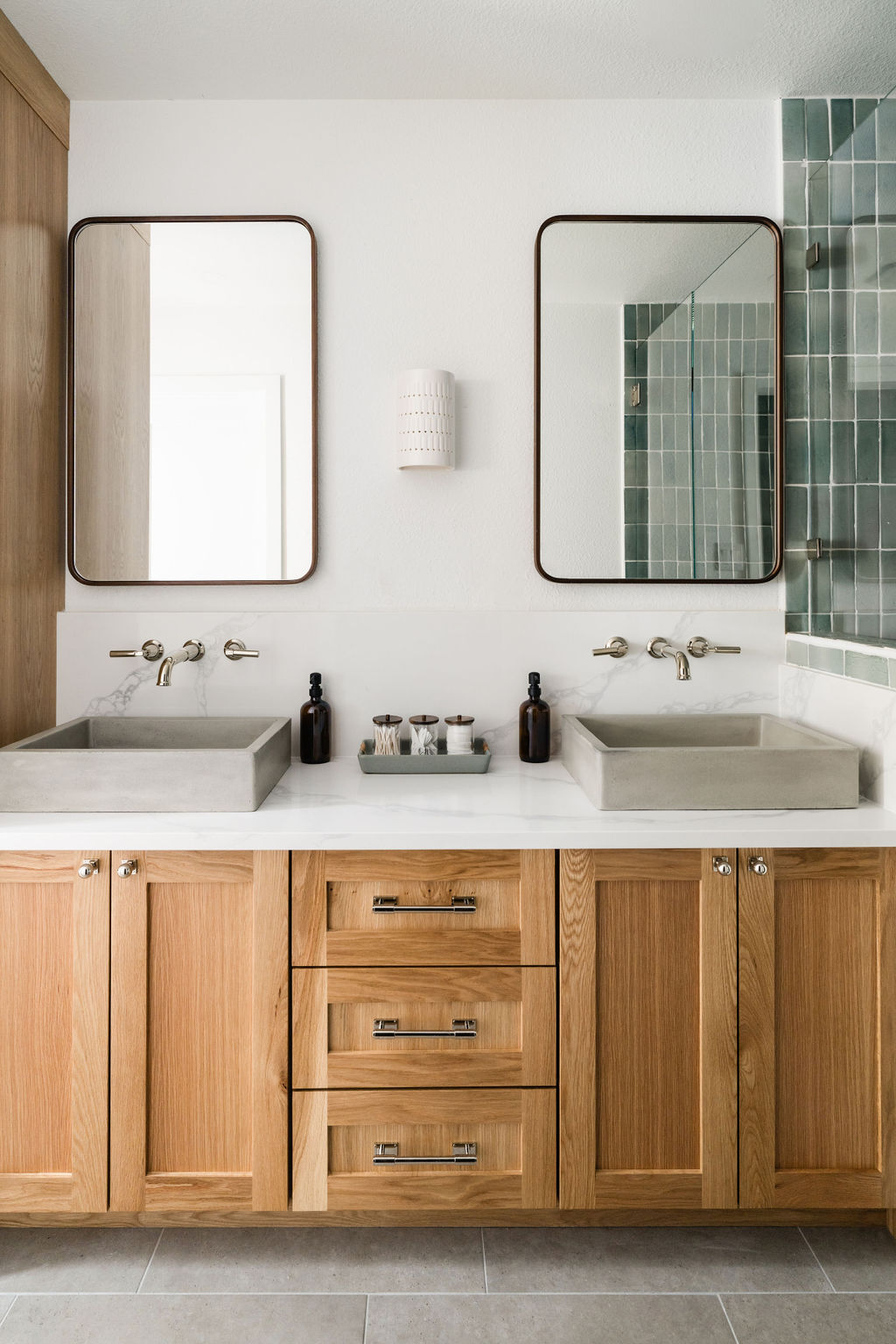 White oak vanity with concrete sinks, wall mounted faucets, and green tile.