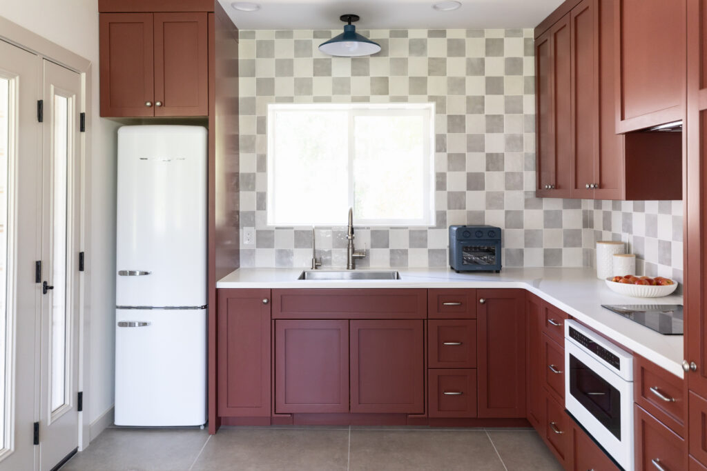 Accessible casita kitchen with roll under sink, checkerboard backsplash, red cabinets, and grey tile floors. 