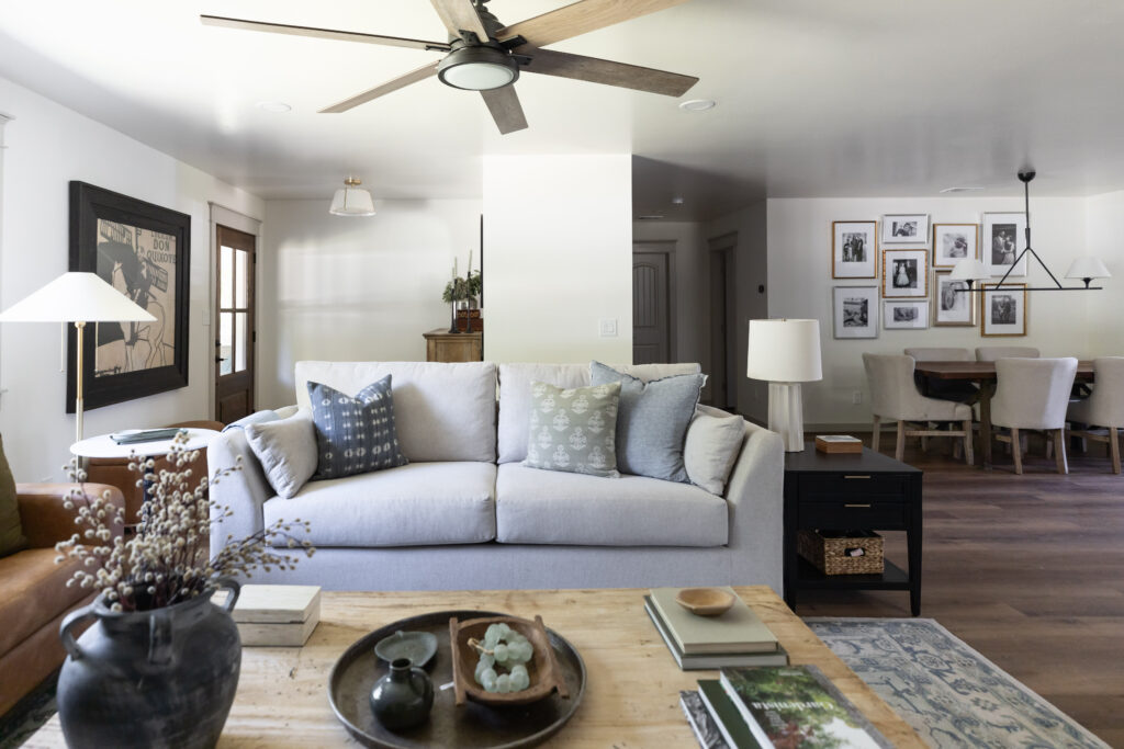 Cozy living room with light sofa, throw pillows, and a dining area behind with a gallery wall