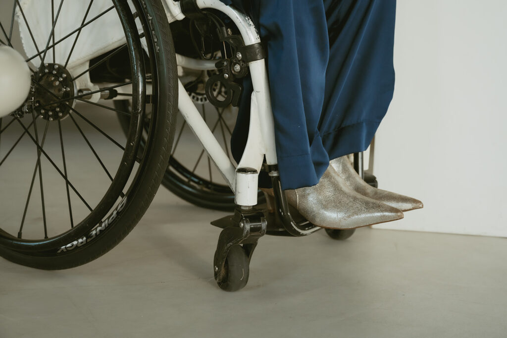 Close-up of a wheelchair with a person wearing metallic silver boots and navy pants, symbolizing the curb cut effect and inclusive design and accessibility empowerment.