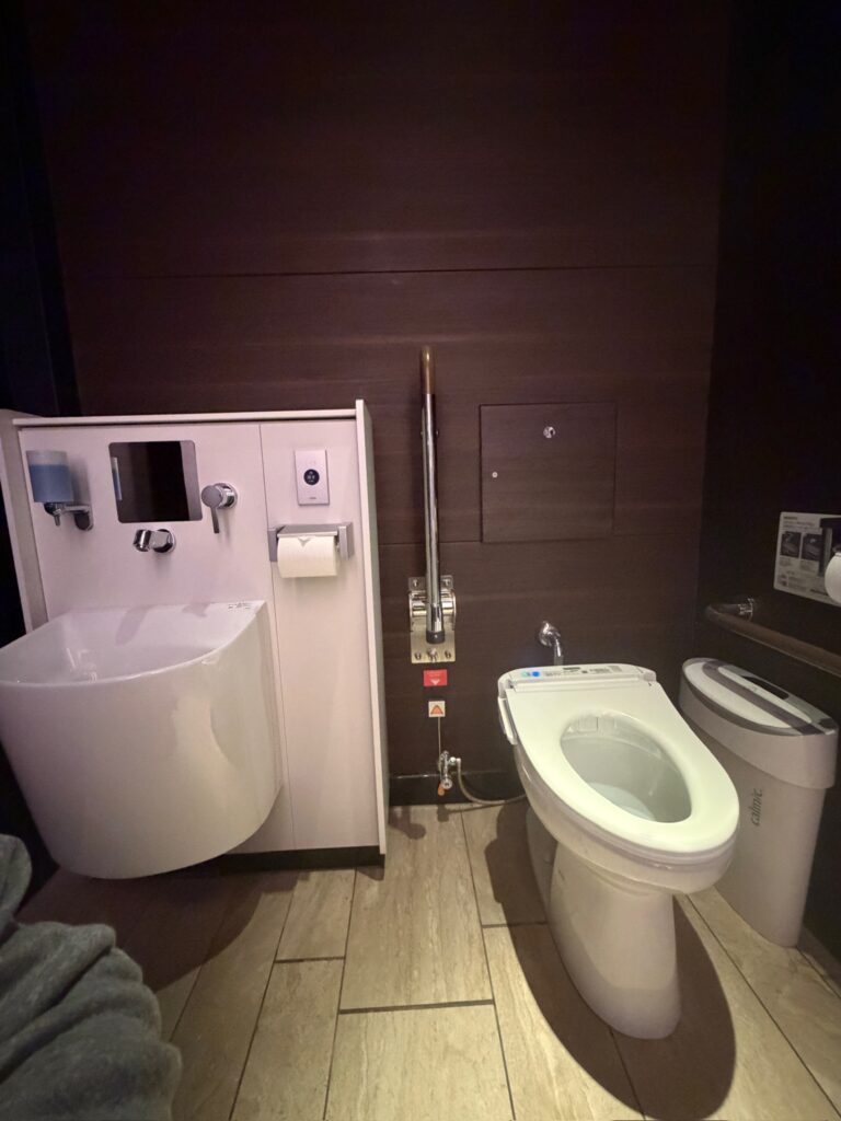 Accessible restroom design in Japan featuring a wall mounted sink, bidet toilet, grab bars, and open floor space to support wheelchair users and inclusive, barrier free bathroom layouts.