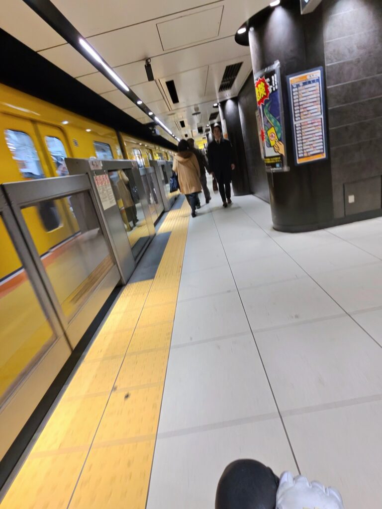 Accessible Tokyo subway platform with a yellow tactile guidance strip, platform screen doors, level boarding area, and wide circulation space supporting wheelchair users and inclusive public transportation design.